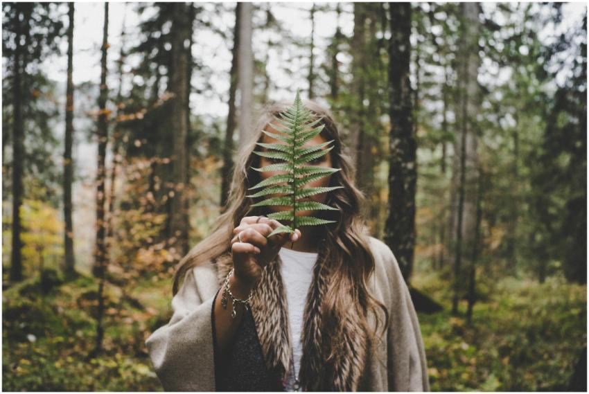 Woman holding a fern leaf in a vibrant autumn fore