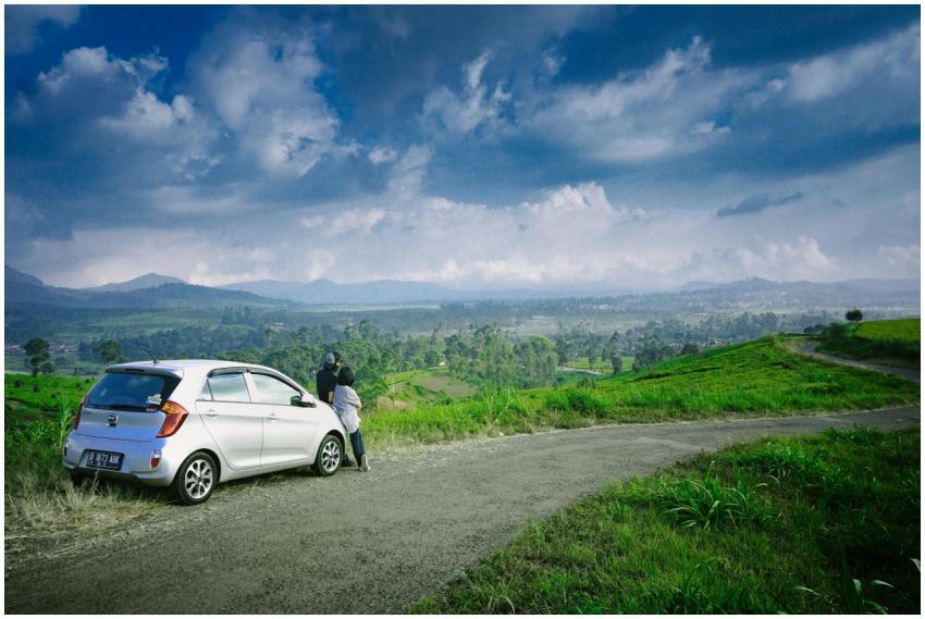 A couple stands by their car on a road overlooking