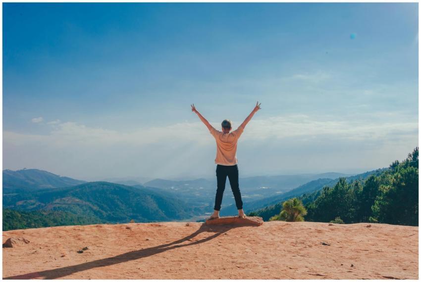 A woman stands victoriously on a mountain top with