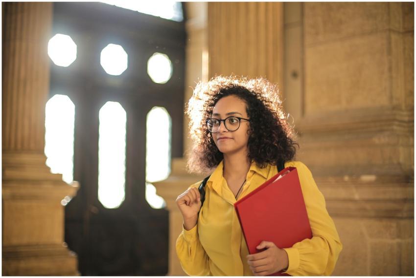 A young woman in a library carrying a red binder,