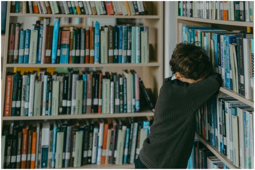 Young boy in a library, resting against a bookshel