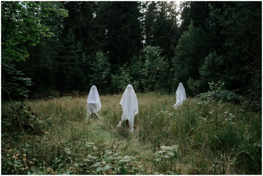 Three people dressed as ghosts in a forest setting