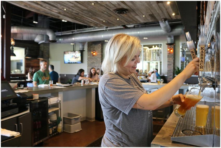 A smiling bartender pours a beer for customers in