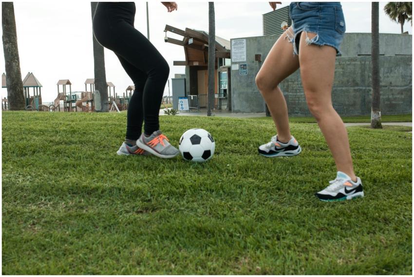 Two women playing soccer on grass in a park settin