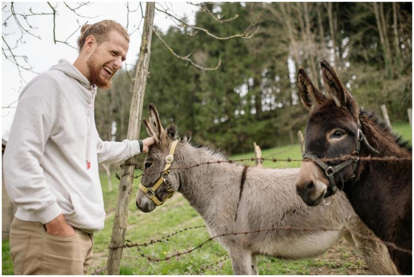 A smiling man pets a donkey through a fence on a r