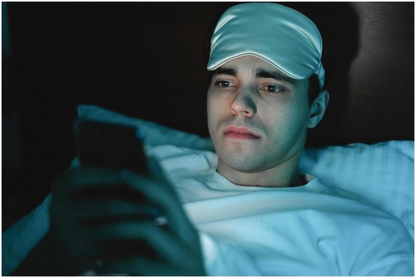A man wearing a sleeping mask uses his smartphone