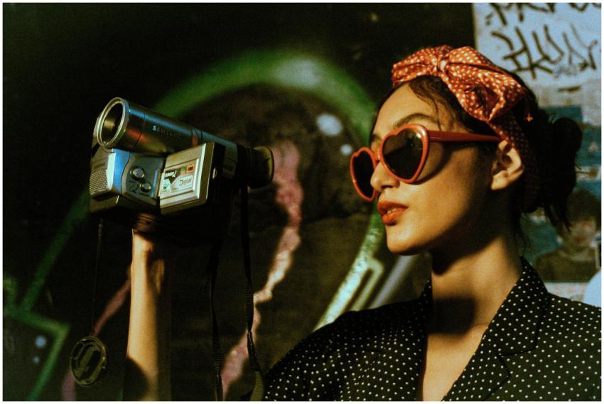 Woman in polka dot attire filming with a vintage c