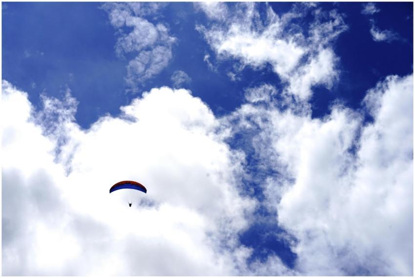 A paraglider soars through a bright blue sky fille