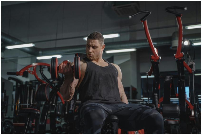 Athletic man performing dumbbell curls while sitti
