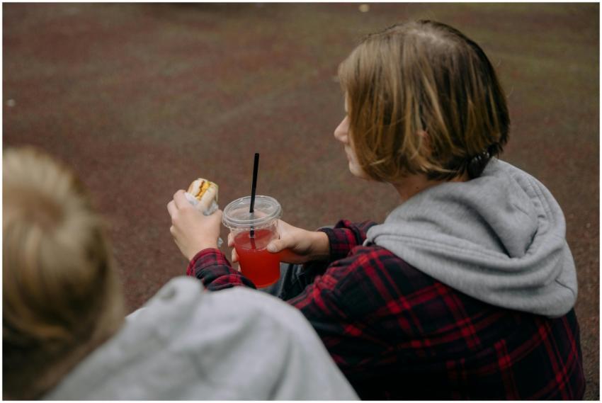 Teen holding a burger and drink outdoors, enjoying