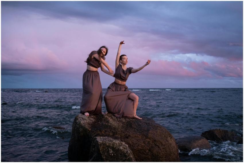Two women gracefully dancing on rocks by the ocean