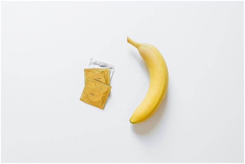 A yellow banana next to packaged condoms on a whit