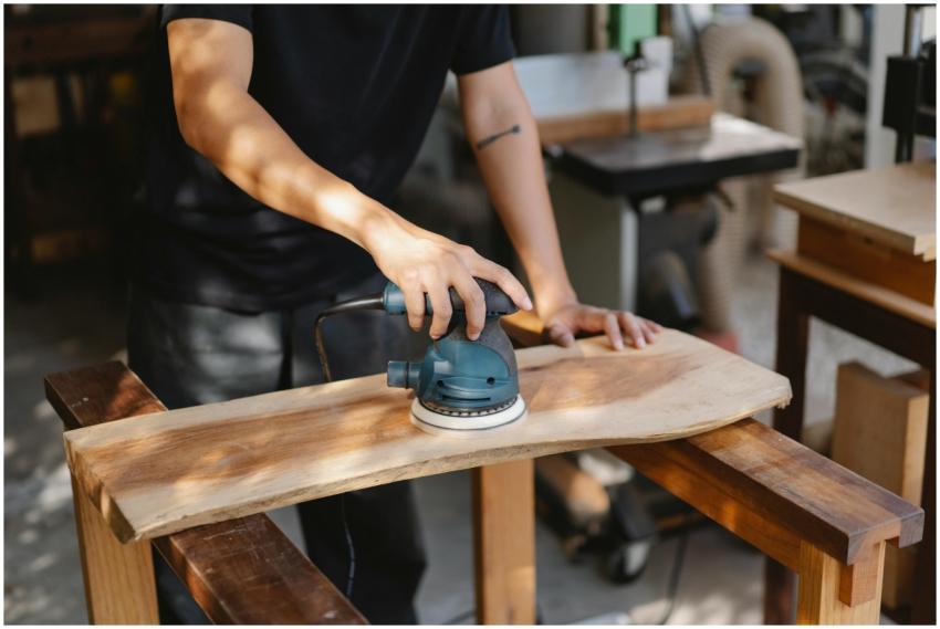 A craftsman uses a power sander on a wooden plank