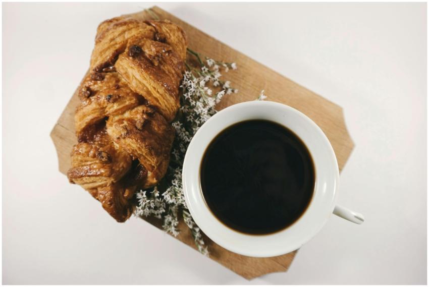 A cup of black coffee and flaky croissant on a woo