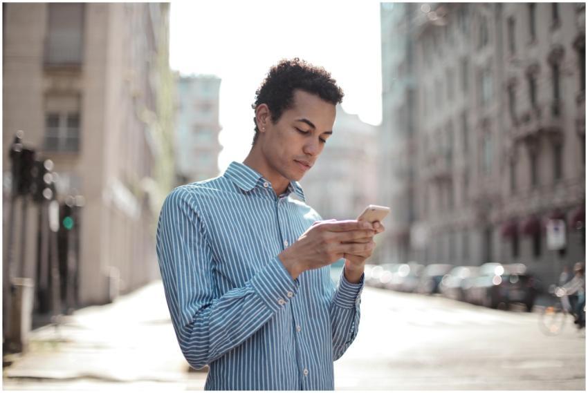 A young man stands outdoors in a city street, focu