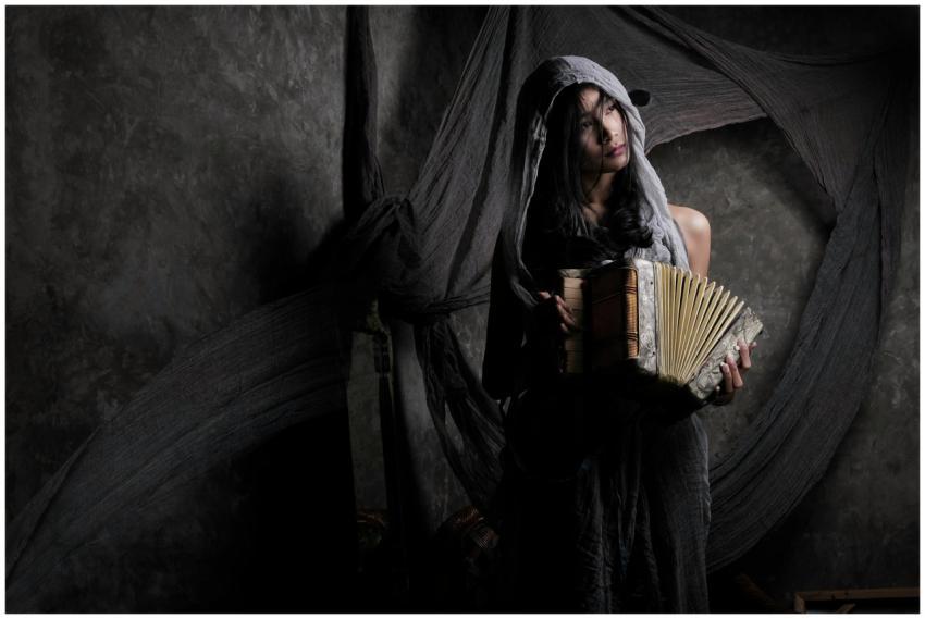 A woman in a veil plays an accordion in a dimly li