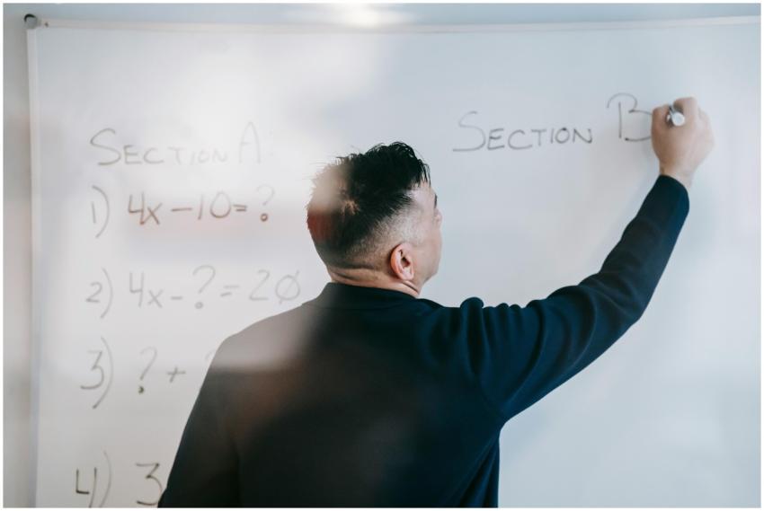 A male teacher writes equations on a whiteboard du