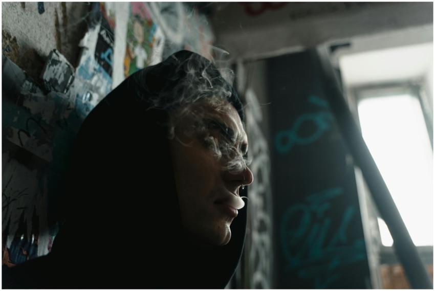 Person in hoodie surrounded by graffiti, exhaling