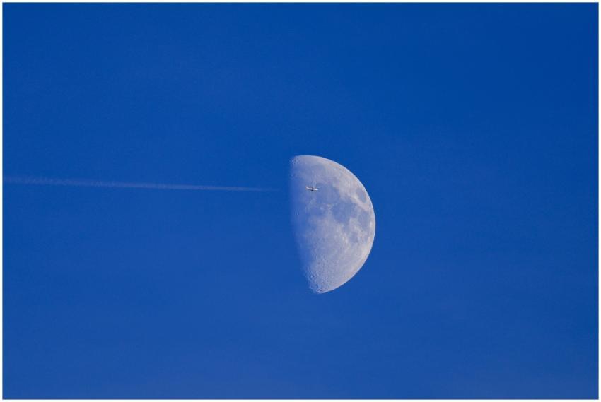 Airplane flying past a half moon against a bright