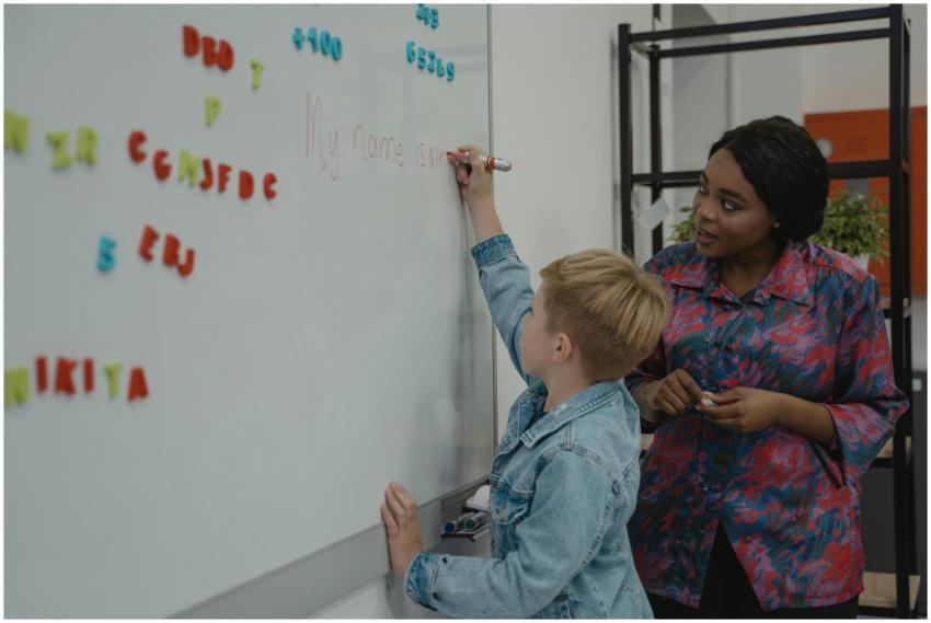 A teacher guides a student writing on a classroom