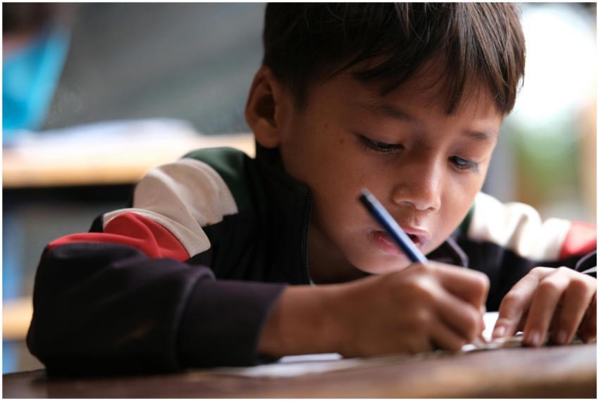 A young boy intently writing in a classroom settin