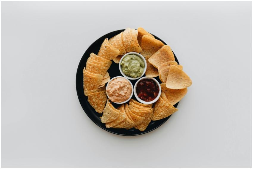 Top view of tortilla chips with guacamole, salsa,