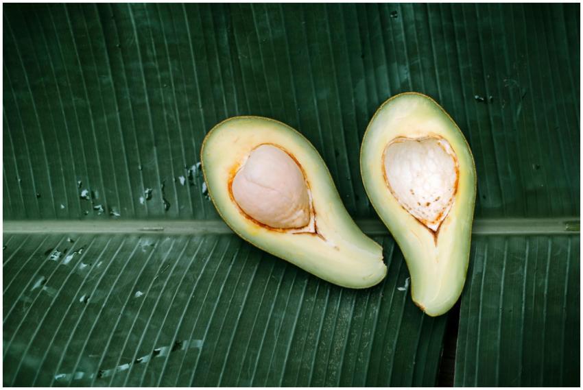 Fresh avocado halves displayed on a banana leaf, h