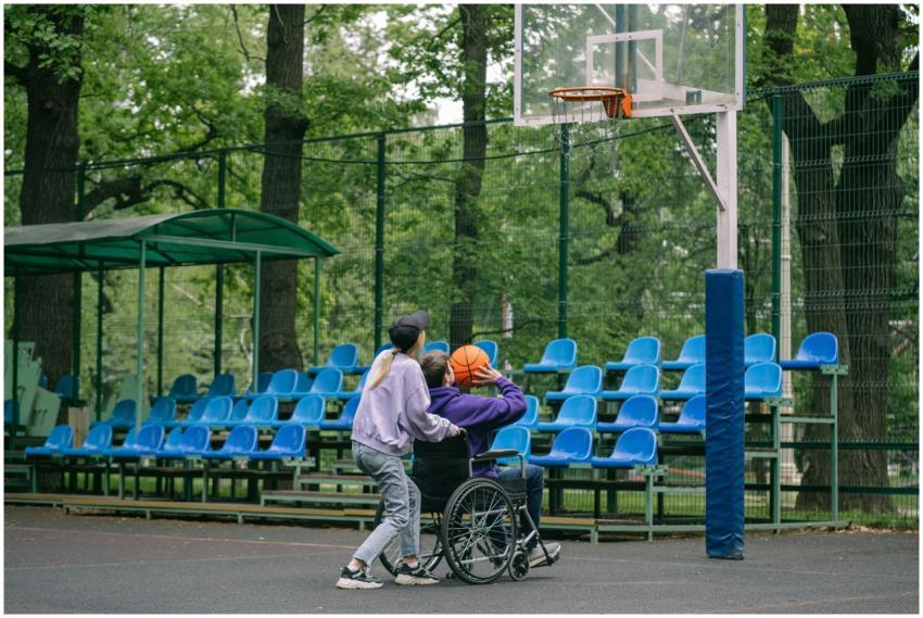 A person assists a wheelchair user to shoot a bask