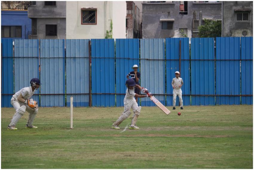 Action shot of teenagers playing cricket on a gras