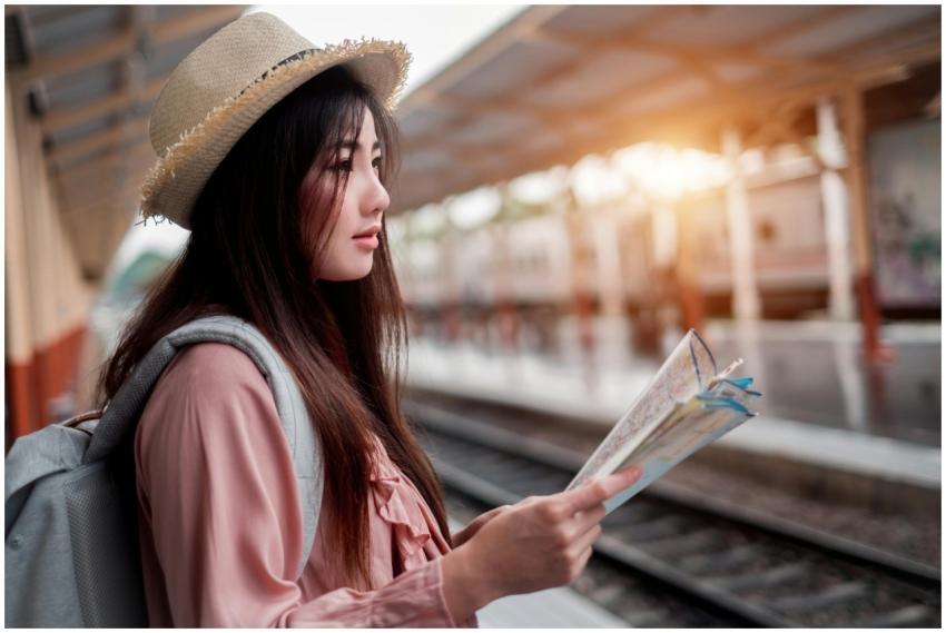 A stylish woman with a map at a train station, rea