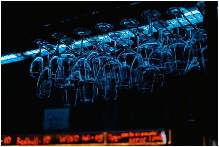Racks of wine glasses hang in a dimly lit bar, ill