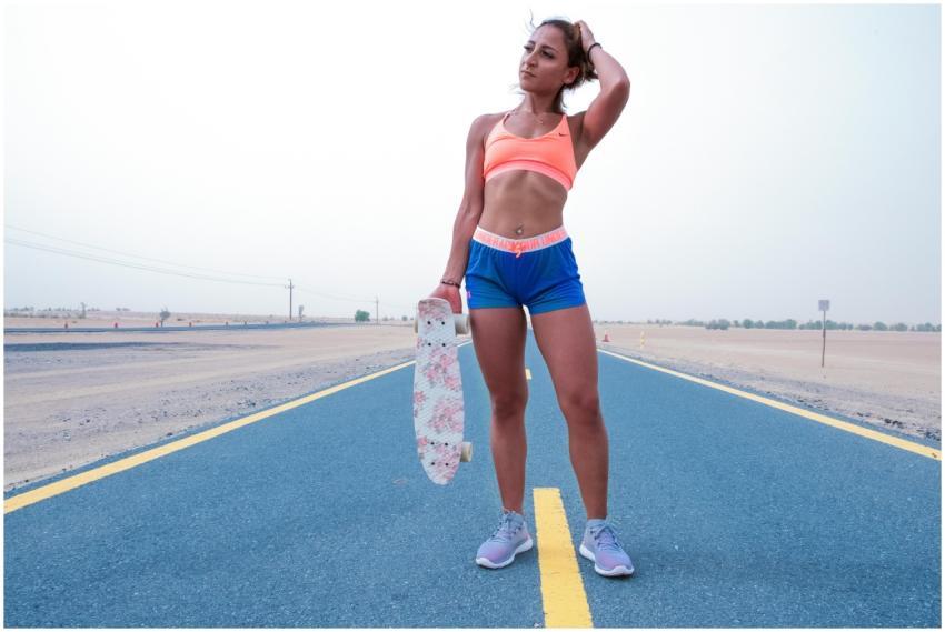 Fit young woman in sportswear holding skateboard o