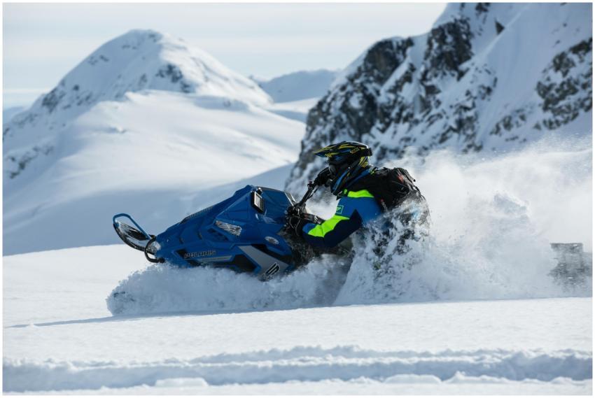 A man on a snowmobile rides through a snowy mounta