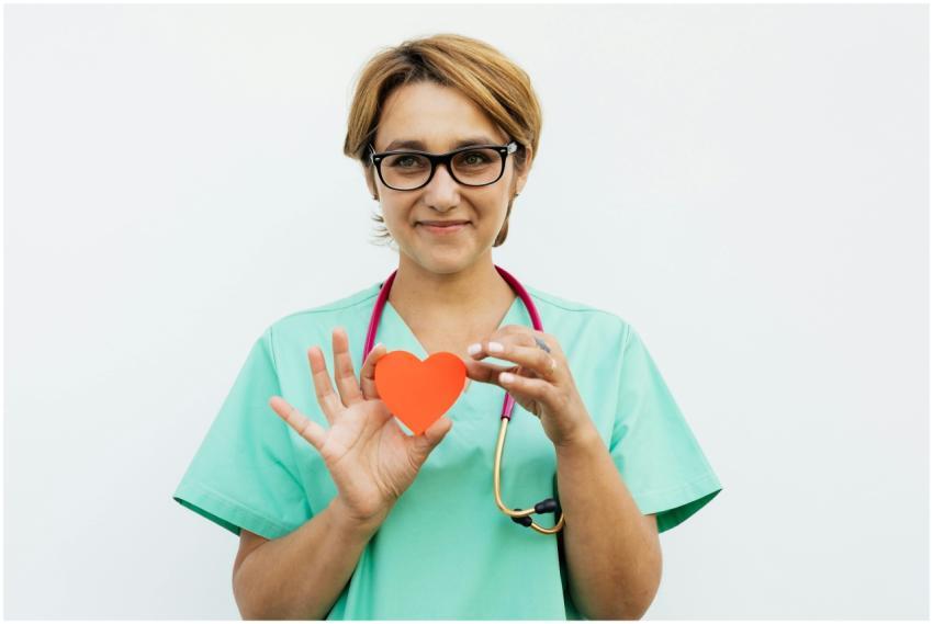 Female doctor in scrubs holding a paper heart symb