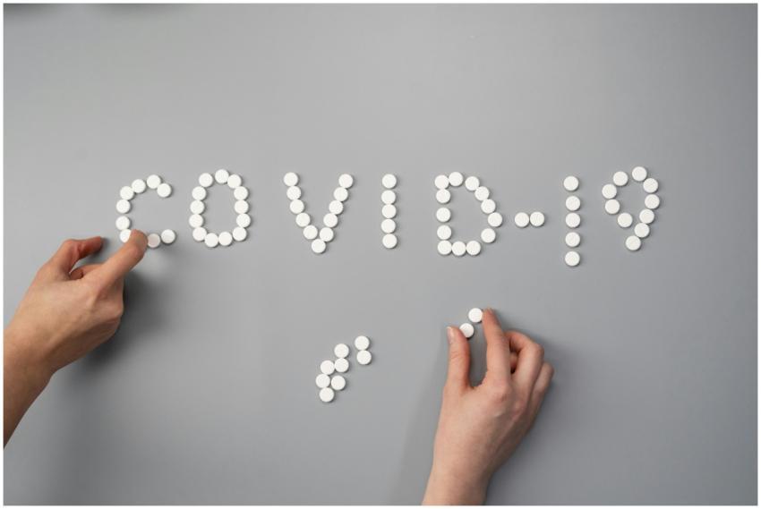 Hands arranging white pills to spell 'COVID-19' on