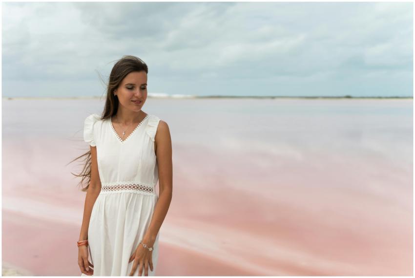 A woman standing by a serene pink lake wearing a w
