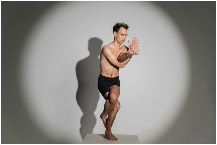 A shirtless man meditating in a balanced yoga pose