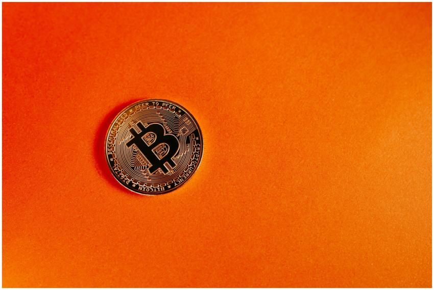 Close-up of a Bitcoin coin on a vivid orange backg