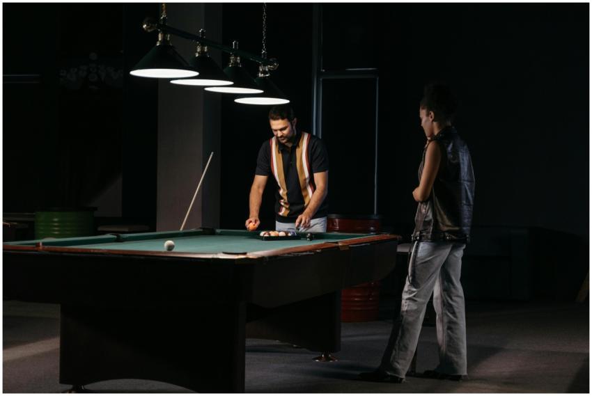 Two adults playing billiards in a dimly lit room,