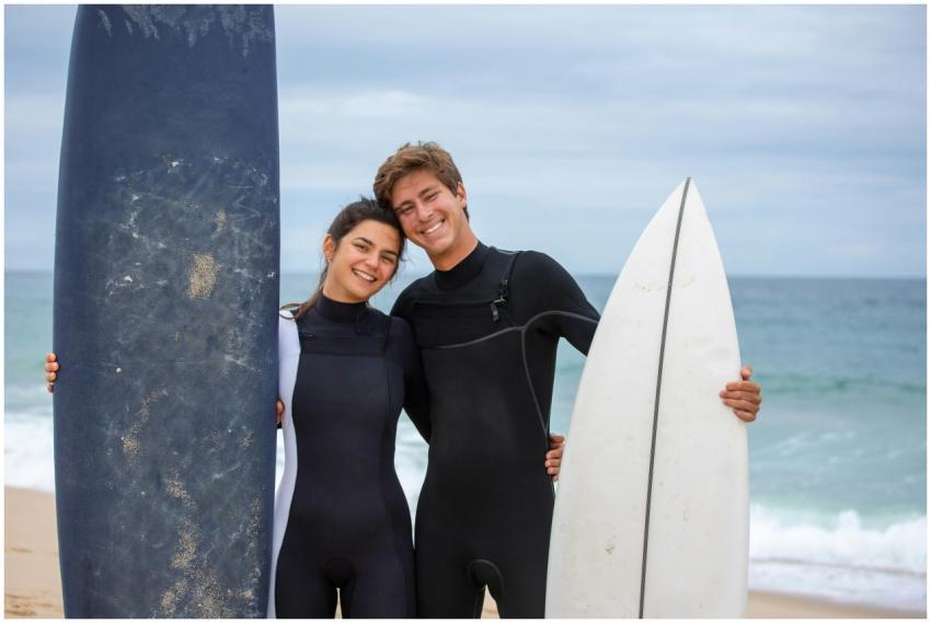 A joyful couple in wetsuits holding surfboards on