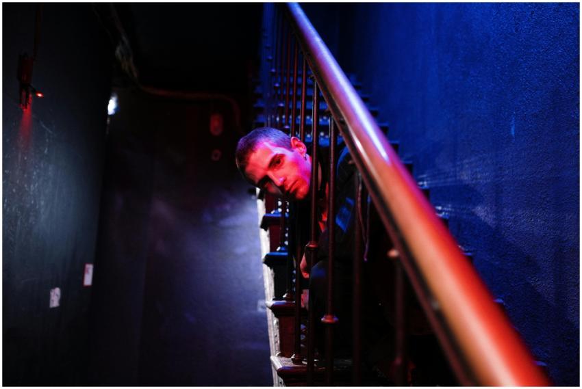 A man leans on a staircase railing under dramatic