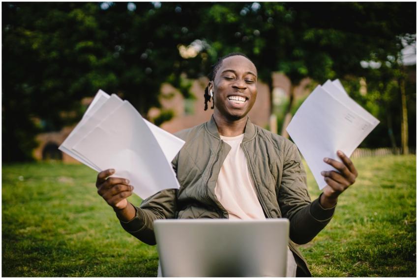 Happy young man holding papers with a laptop outdo