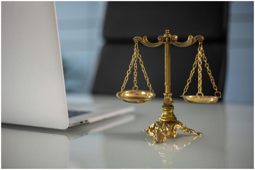 Golden justice scales on a desk beside a laptop, s