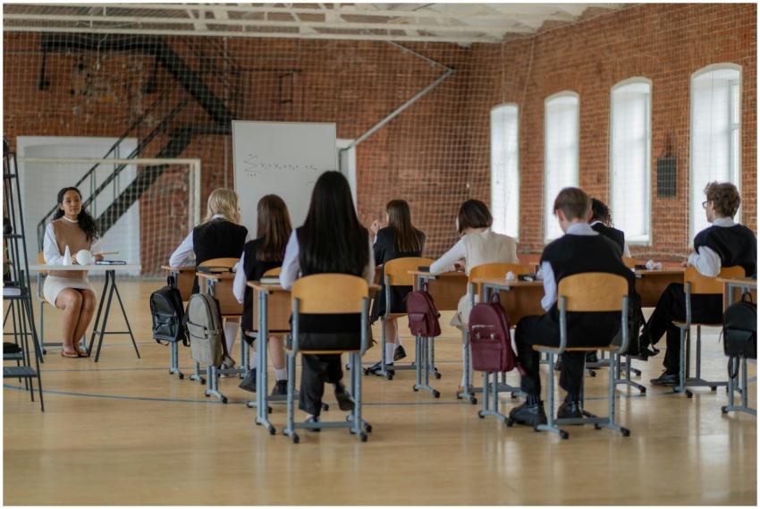 Students in a classroom setting facing a teacher,