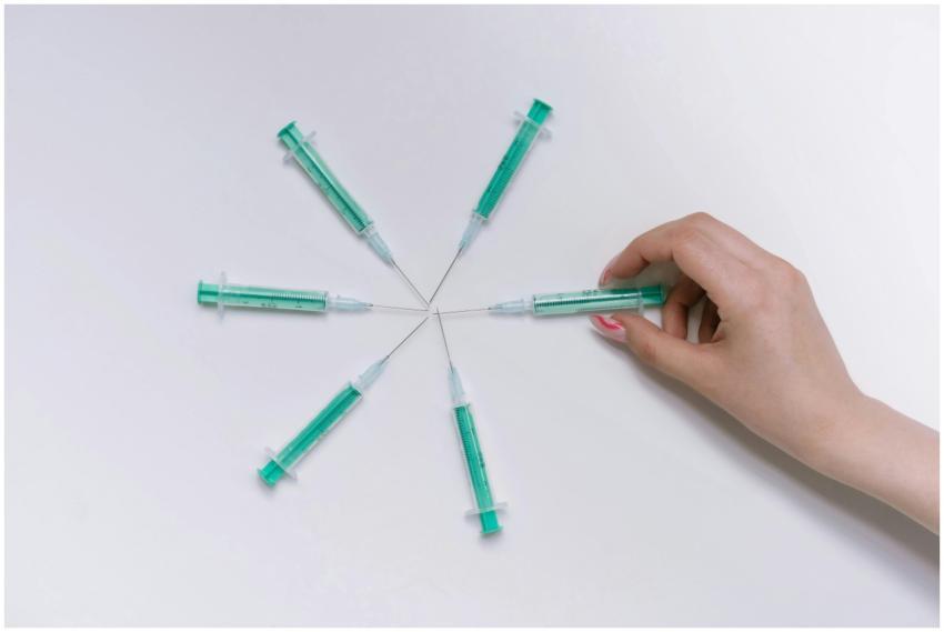 A hand arranges green syringes in a circular patte
