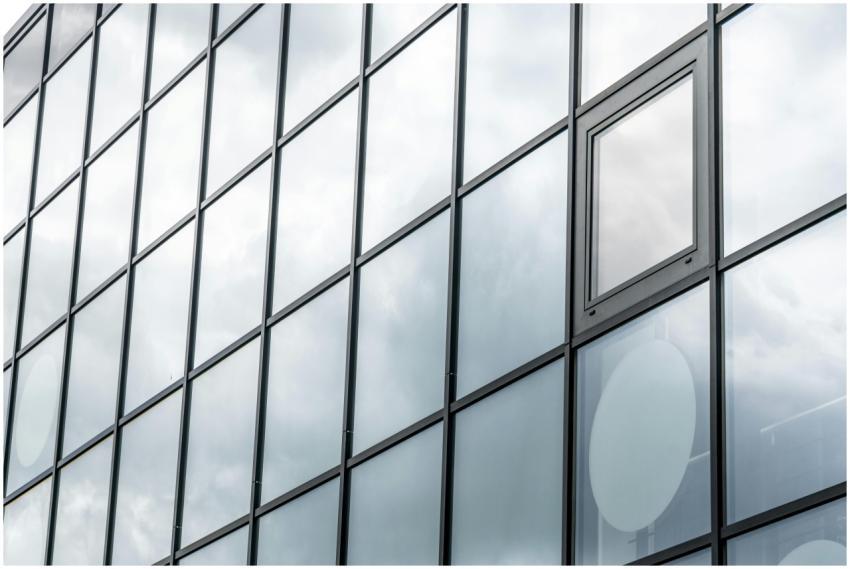 A modern glass facade reflecting a cloudy sky, sho