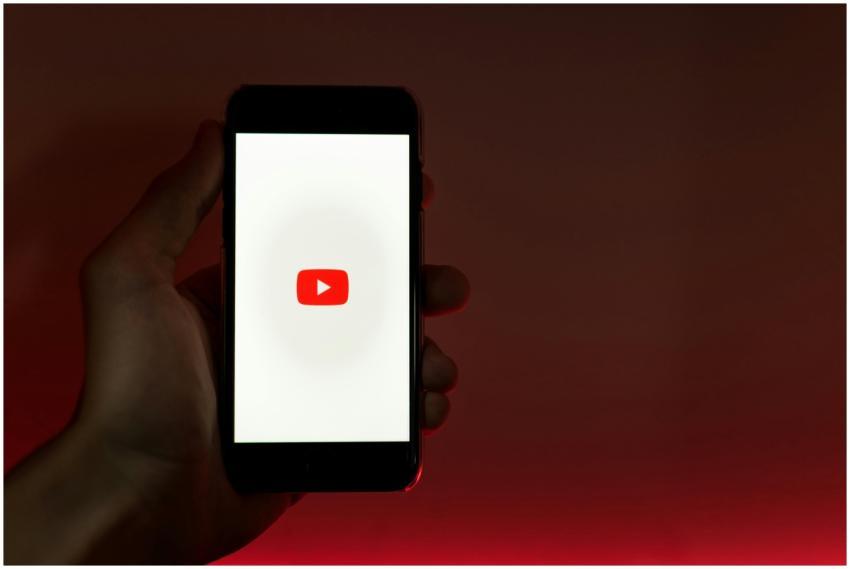A hand holding a smartphone displaying the YouTube