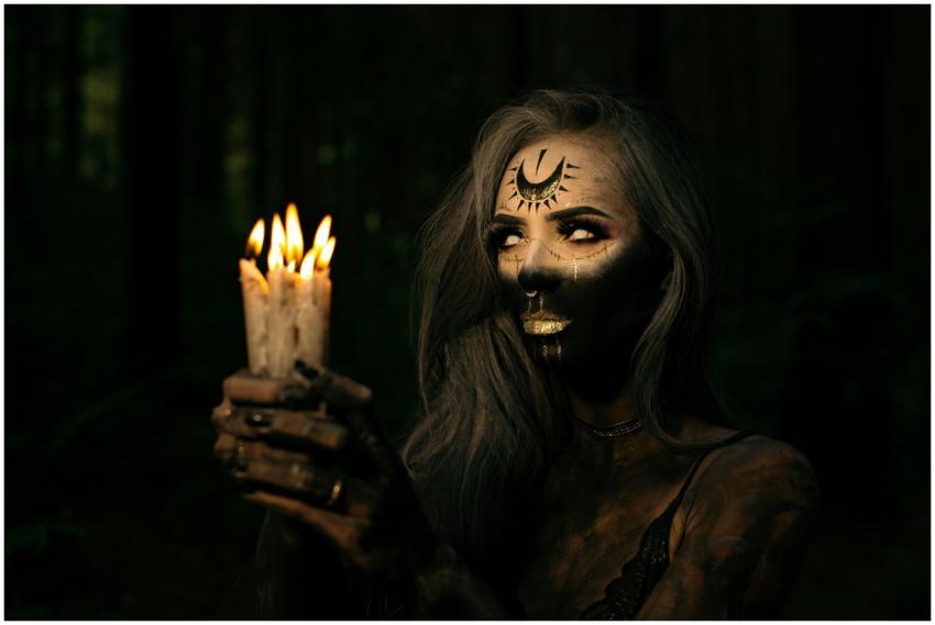 A mysterious woman with face paint holds lit candl