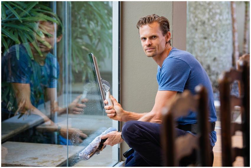 A man in a blue t-shirt cleaning large glass pane