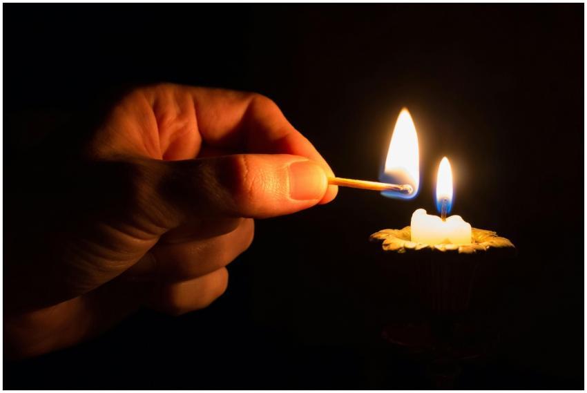 A hand uses a match to light a candle in a dimly l